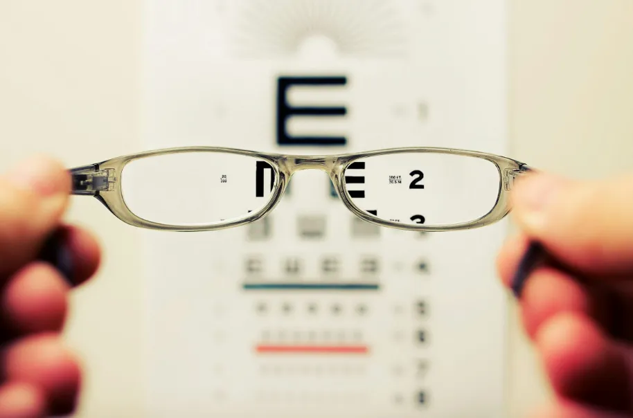 Hands holding up a pair of glasses to a vision test